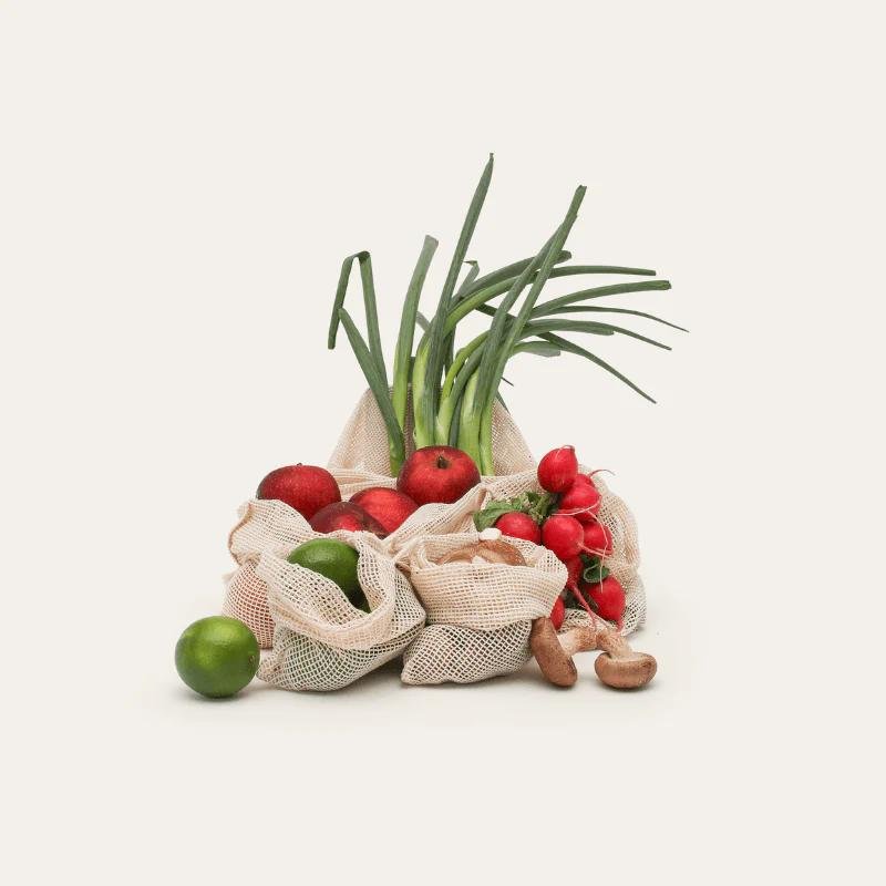 Fresh produce in eco-friendly mesh bags — radishes, lime, apples, spring onions, mushrooms