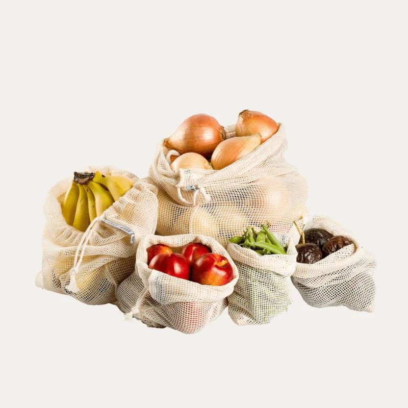 Assortment of fresh produce in eco-friendly mesh bags — bananas, onions, apples, peppers, dates