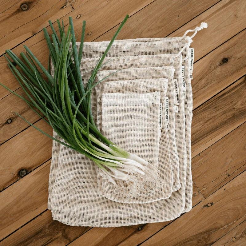 Fresh spring onions on a wooden surface beside reusable mesh produce bags